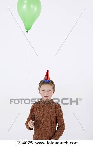 A serene boy wearing a party hat and holding a balloon, close-up View Large Photo Image Stock Photography - A serene boy wearing a party hat and holding a balloon, close-up. Fotosearch