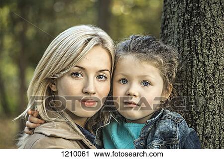 A serene looking mother and her young daughter next to a tree trunk View Large Photo Image Stock Image - A serene looking mother and her young daughter next to a tree trunk. Fotosearch