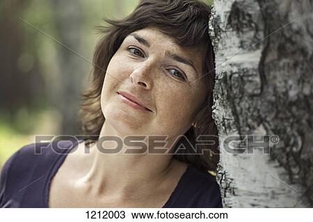 A serene woman leaning against a tree trunk View Large Photo Image Stock Image - A serene woman leaning against a tree trunk. Fotosearch