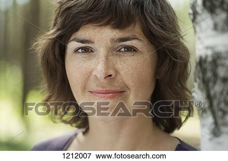Stock Photo - A serene woman standing next to a tree trunk. Fotosearch