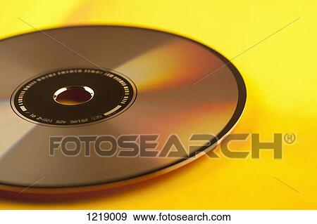 Stock Photo - A single compact disc on a yellow background, close-up. Fotosearch