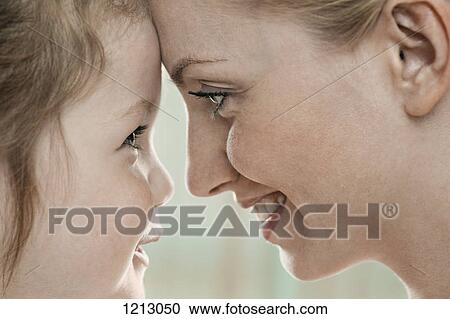 Stock Image - A smiling mother and daughter touching foreheads, close-up. Fotosearch