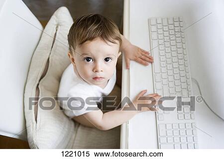 Stock Photography - A toddler sitting at a desk with a computer keyboard. Fotosearch