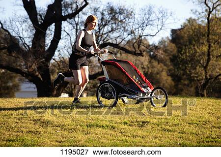 Stock Photo - A woman running in a park and pushing a pram. Fotosearch