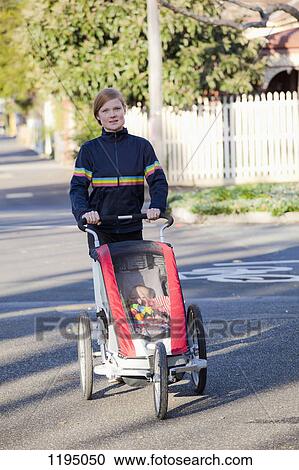 A woman walking on a street and pushing a baby stroller View Large Photo Image Stock Image - A woman walking on a street and pushing a baby stroller. Fotosearch