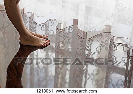 Stock Image - A woman's bare feet on a shiny hardwood floor. Fotosearch