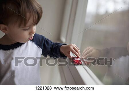 Stock Photo - A young boy pushing a toy car along a window sill. Fotosearch