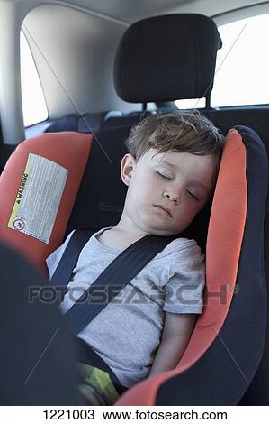 Stock Image - A young boy sleeping in a car seat in the back seat of a car. Fotosearch