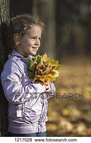 A young cheerful girl holding a bunch of autumn leaves with pride View Large Photo Image Stock Photo - A young cheerful girl holding a bunch of autumn leaves with pride. Fotosearch