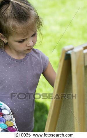 A young girl concentrating seriously while she's painting on an easel View Large Photo Image Stock Photography - A young girl concentrating seriously while she's painting on an easel. Fotosearch