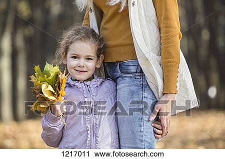 A young girl holding a bouquet of autumn leaves and holding onto her Mom View Large Photo Image Stock Image - A young girl holding a bouquet of autumn leaves and holding onto her Mom. Fotosearch