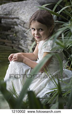 A young girl in a white dress sitting in nature View Large Photo Image Stock Image - A young girl in a white dress sitting in nature. Fotosearch