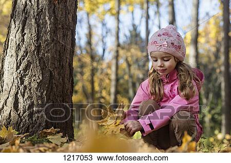 Stock Image - A young girl picking up autumn leaves in a wooded area. Fotosearch