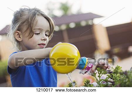 Stock Photo - A young girl watering a flower with a toy watering can. Fotosearch