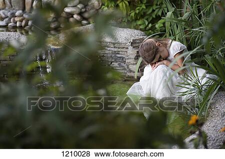 Stock Photo - A young sad girl resting her head on her hands while sitting by a pond. Fotosearch