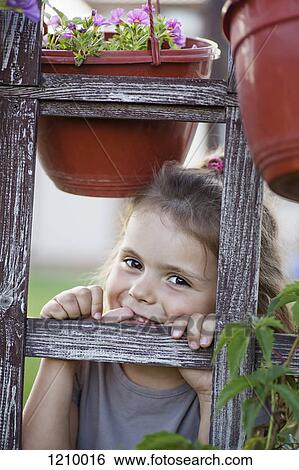 Stock Photograph - A young smiling girl looking through a trellis. Fotosearch