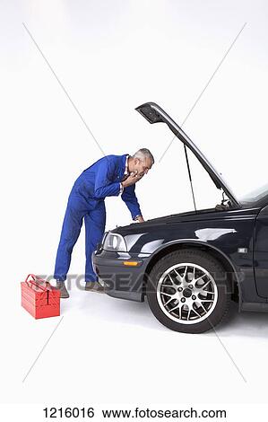 Stock Photograph - An auto mechanic looking under the hood of a car with uncertainty. Fotosearch