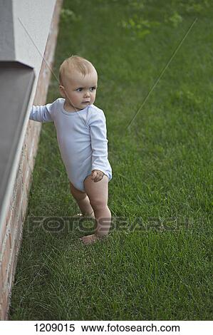 Stock Photography - Baby in garden leaning against wall. Fotosearch
