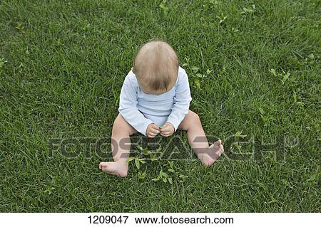 Stock Photo - Baby playing with leaves on the grass. Fotosearch