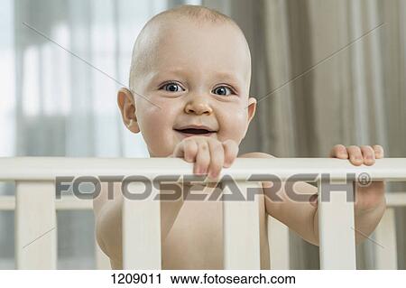 Stock Image - Baby standing in cot. Fotosearch