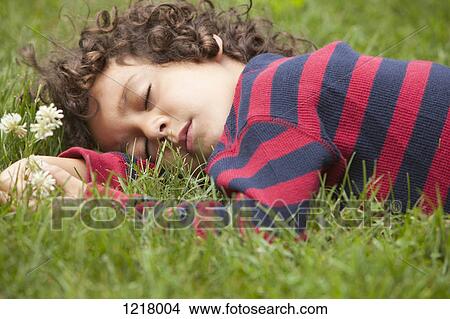 Picture - Boy sleeping on grass holding flowers. Fotosearch