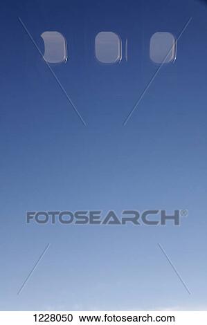 Stock Image - Clear blue sky and windows seen in reflection of airplane window. Fotosearch
