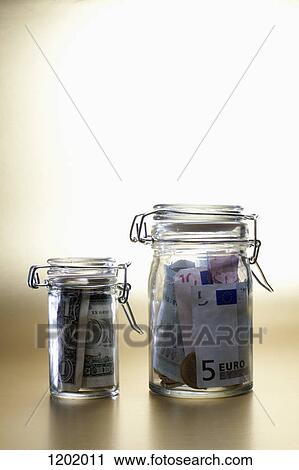 Stock Image - Dollar in a little jar beside larger jar full of euros. Fotosearch