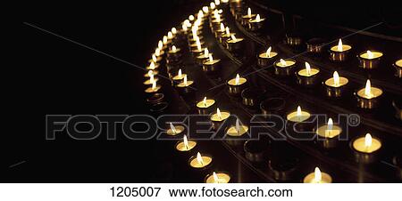Many lit votive candles in a row against a black background View Large Photo Image Stock Photo - Many lit votive candles in a row against a black background. Fotosearch
