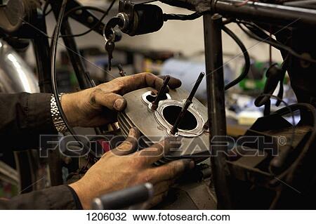 Stock Image - Mechanic attaching cylinder to motorcycle. Fotosearch