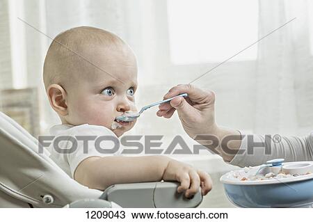 Stock Image - Mother spoon feeding her baby. Fotosearch