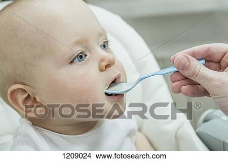 Mother spoon feeding her son on high chair View Large Photo Image Picture - Mother spoon feeding her son on high chair. Fotosearch