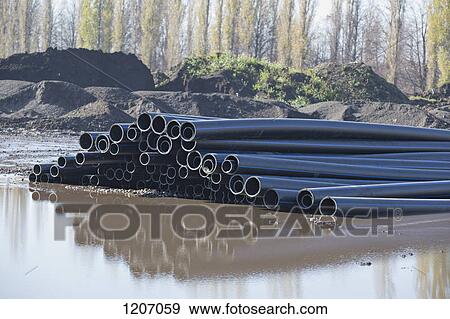 Stock Photo - Plastic pipes reflected in water at construction site. Fotosearch
