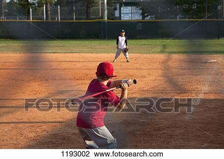 Stock Image - Rear view of a boy preparing to swing a bat on baseball diamond. Fotosearch