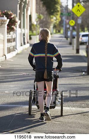 Stock Photo - Rear view of a woman walking on a sidewalk with a pram. Fotosearch