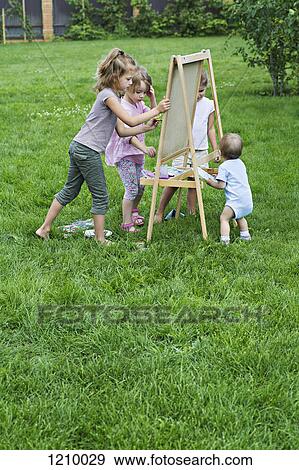 Three young girls and a toddler painting outdoors on an easel View Large Photo Image Stock Photo - Three young girls and a toddler painting outdoors on an easel. Fotosearch