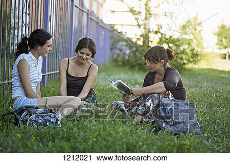 Two friends in a park listening to their friend read from a book View Large Photo Image Stock Image - Two friends in a park listening to their friend read from a book. Fotosearch