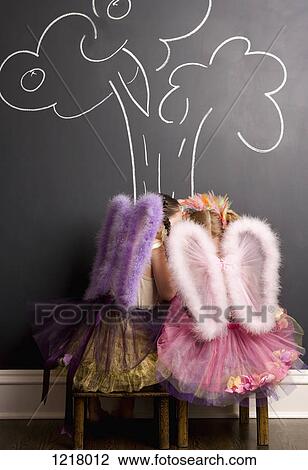 Stock Image - Two girls dressed as angels in front of blackboard with image of tree. Fotosearch
