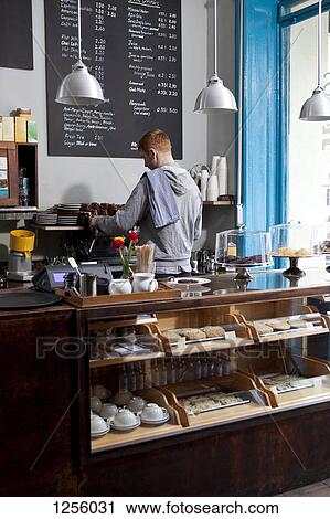 Stock Image - A barista working at an espresso maker in a cafe, rear view. Fotosearch