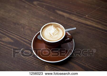 Stock Image - A cafe latte with a floral pattern in the milk froth on a table in a cafe. Fotosearch