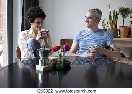 Stock Image - A cheerful hip mixed age couple enjoying breakfast together in their dining room. Fotosearch