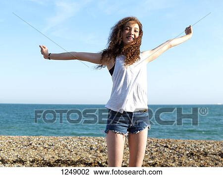 A cheerful teenage girl standing on the beach with her arms raised in exhilaration View Large Photo Image Stock Image - A cheerful teenage girl standing on the beach with her arms raised in exhilaration. Fotosearch