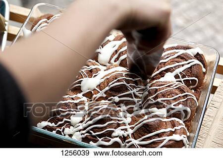 Stock Photo - A coffee shop employee cutting into a pan of cinnamon rolls. Fotosearch