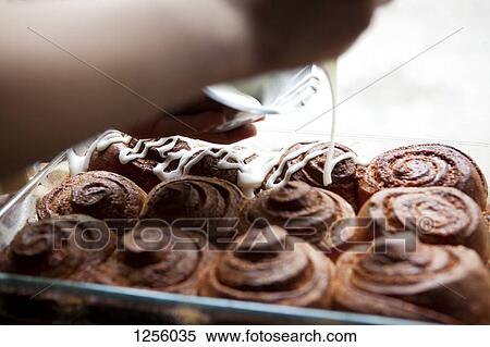 Stock Photography - A coffee shop employee frosting cinnamon rolls with icing. Fotosearch