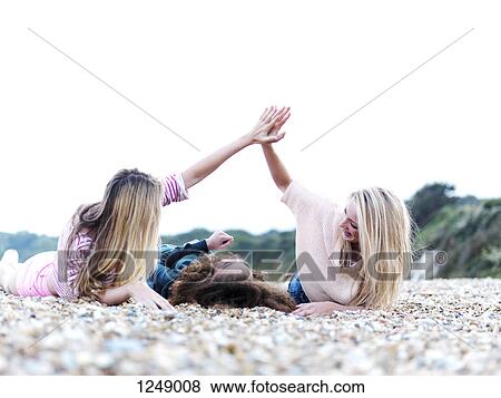 A girl lying in between two friends high-fiving above her at the beach View Large Photo Image Stock Photo - A girl lying in between two friends high-fiving above her at the beach. Fotosearch