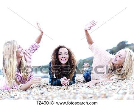 Stock Photo - A girl lying in between two friends high-fiving above her at the beach. Fotosearch