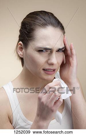 A grimacing young woman holding a tissue with her hand to her temple View Large Photo Image Stock Photo - A grimacing young woman holding a tissue with her hand to her temple. Fotosearch