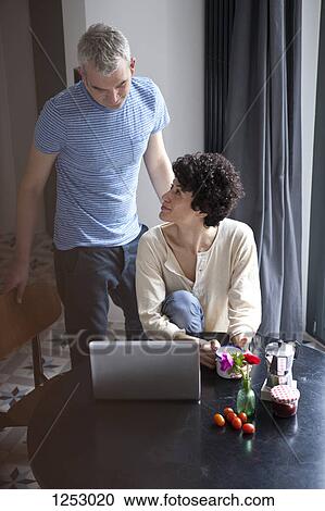 A hip mixed age couple using a laptop at the dining table View Large Photo Image Stock Image - A hip mixed age couple using a laptop at the dining table. Fotosearch