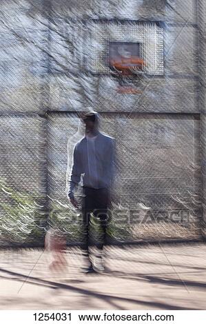 Stock Image - A hip young man dribbling a basketball at a public outdoor court. Fotosearch
