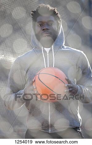 A hip young man holding a basketball and standing on an outdoor basketball court View Large Photo Image Stock Photo - A hip young man holding a basketball and standing on an outdoor basketball court. Fotosearch