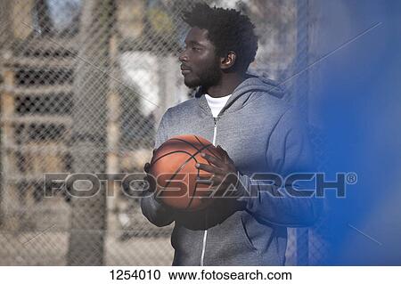 Stock Image - A hip young man looking away thoughtfully while holding a basketball. Fotosearch